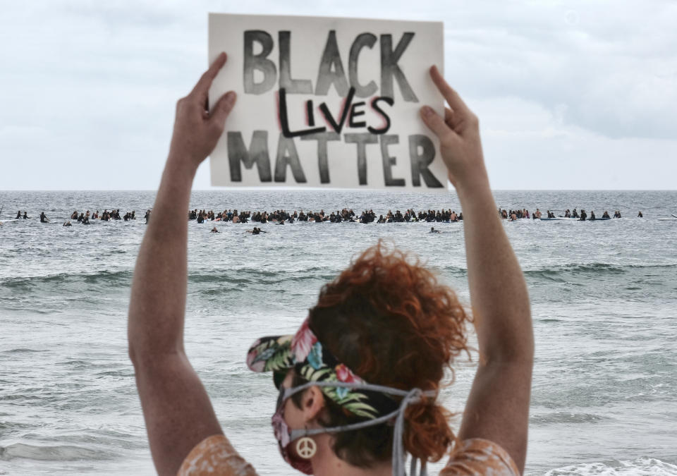 FILE - In this June 5, 2020, file photo, Shawna Ventimiglia from Manhattan Beach holds a sign in support of a local group of surfers during a traditional paddle out ceremony in Hermosa Beach in support of Black Lives Matter over the death of George Floyd in Los Angeles. The Black Lives Matter Global Network Foundation, which grew out of the creation of the Black Lives Matter movement, is formally expanding a $3 million financial relief fund that it quietly launched in February 2021, to help people struggling to make ends meet during the ongoing coronavirus pandemic. (AP Photo/Richard Vogel, File)
