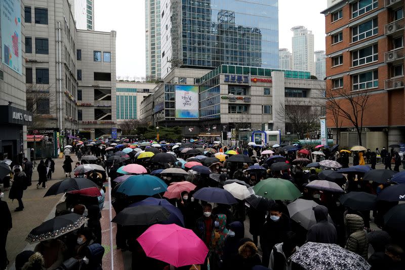 People wearing masks after the coronavirus outbreak wait in a line to buy masks as it rains in front of a department store in Seoul