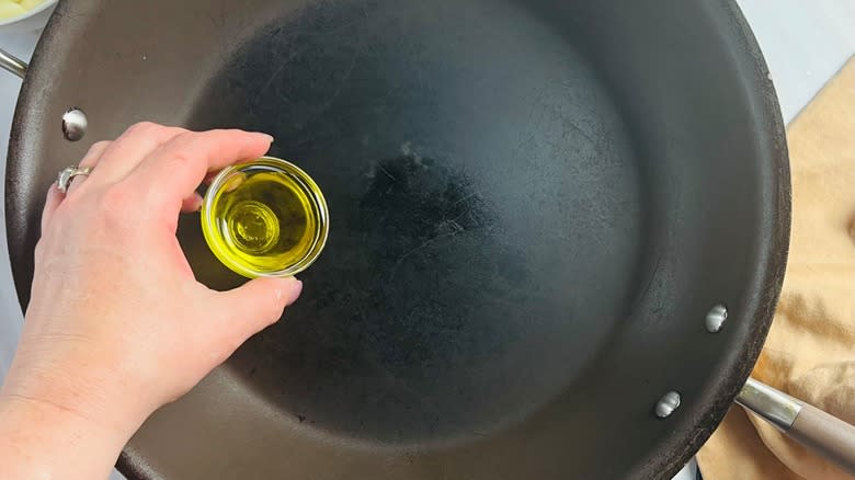 hand pouring oil into pan