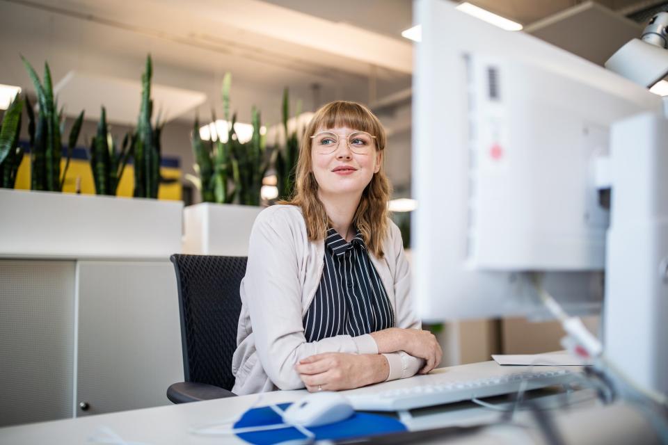 Thoughtful businesswoman looking away while sitting at desk in creative office - Copyright: getty images