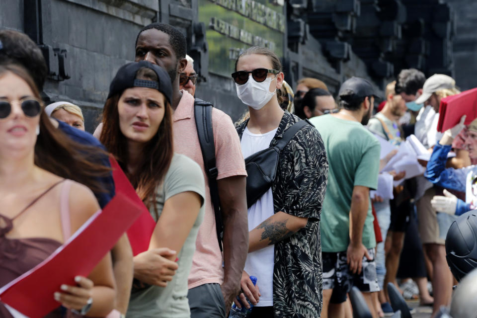 In this March 23, 2020 photo, foreign tourists who are unable to fly home due to the new coronavirus outbreak, queue up outside an immigration office to extend their visas in Bali, Indonesia. Tourists across Asia are finding their dream vacations have turned into travel nightmares as airlines cancel flights and countries close their borders in the fight against the coronavirus pandemic. (AP Photo/Firdia Lisnawati)