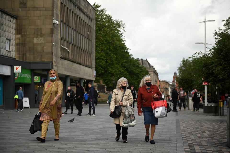 People wear face masks as a precaution against the transmission of COVID-19 as they walk past closed shops in the centre of Bolton, northern England on September 9, 2020, as local lockdown restrictions are put in place due to a spike in cases of the novel coronavirus in the city. - The UK government, which controls health policy in England, imposed tougher restrictions on Bolton, near the northwest city of Manchester, after a "very significant rise" in cases. Bolton was found to have 120 cases per 100,000 people -- the highest in the country. (Photo by Oli SCARFF / AFP) (Photo by OLI SCARFF/AFP via Getty Images)