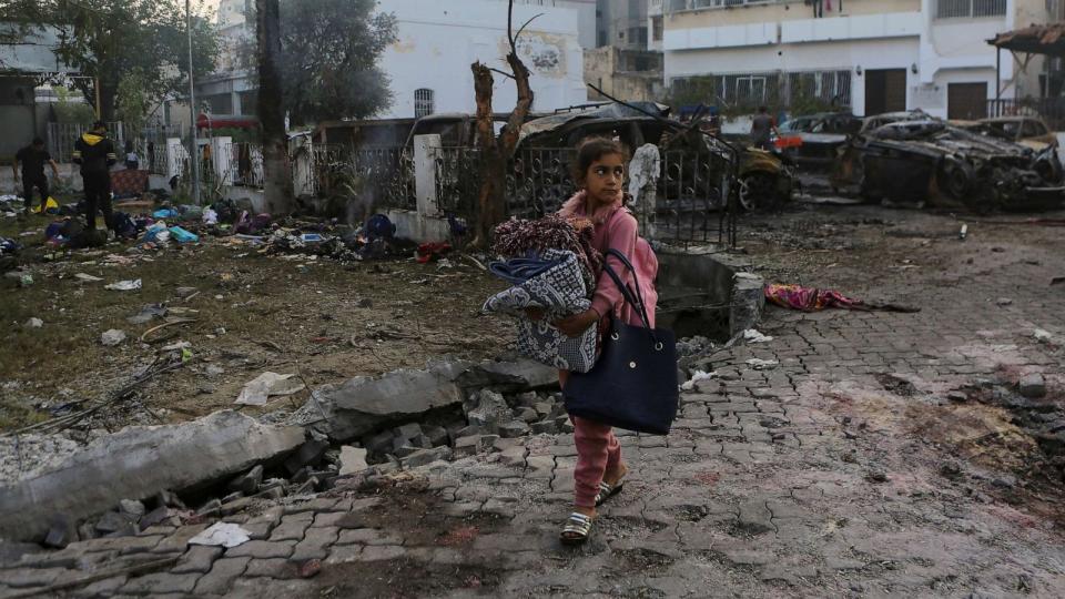 PHOTO: A Palestinian girl carries a blankets as she walks past the site of a deadly explosion at Al Ahli hospital, in Gaza City, Oct. 18, 2023. (Abed Khaled/AP)