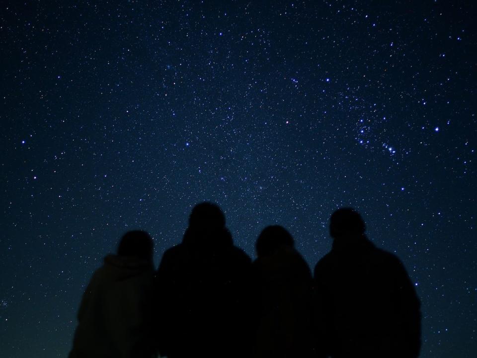 Four people are silhouetted huddling together against the night sky.