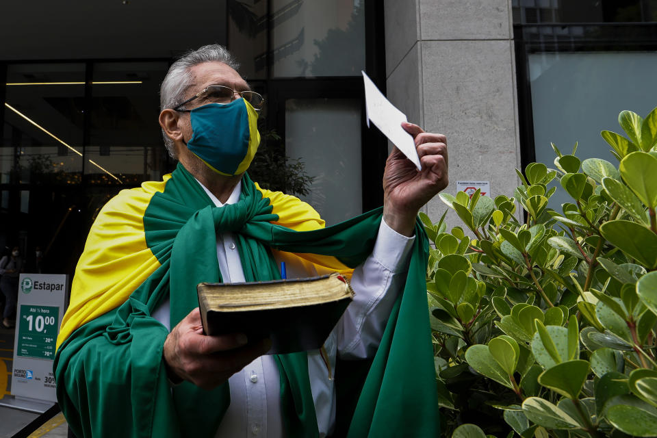 A flag-drapped supporter of Brazilian President Jair Bolsonaro, retired professor of history and geography Antonio Ortega, holds a Bible as he arrives to Vila Nova Star hospital to deliver a letter to the president who is hospitalized in Sao Paulo, Brazil, Monday, Jan. 3, 2022. Bolsonaro is at the hospital Monday for tests after experiencing abdominal discomfort and is in stable condition, according to a hospital statement. (AP Photo/Marcelo Chello)