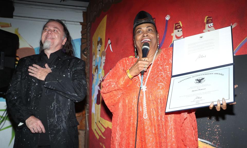 Daytona Beach artist Perego, left, reacts as Khalilah Camacho-Ali shows the crowd a proclamation from President Joe Biden bestowing the Art Army founder with a President's Volunteer Service Lifetime Achievement Award during an award presentation ceremony at The Grind Gastropub & Kona Tiki Bar in Ormond Beach, Tuesday, Jan. 16, 2024. Camacho-Ali is a humanitarian/author/actress once married to boxing legend Muhammad Ali.