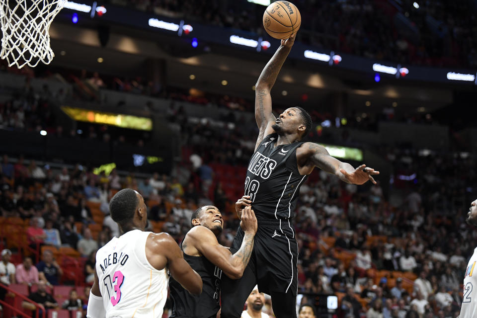 Brooklyn Nets forward Dorian Finney-Smith (28) scores in front of teammate Nic Clayton, center, and Miami Heat center Bam Adebayo (13) during the first half of an NBA basketball game, Saturday, March 25, 2023, in Miami, Fla. (AP Photo/Michael Laughlin)