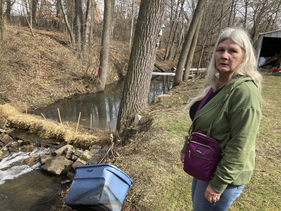 Sherry Bable stands beside Sulphur Run, a creek, Feb. 25, 2023, in East Palestine, Ohio, near the spot where a train derailed in a fiery crash Feb. 3. It's among local waterways where "Keep Out" signs are being posted as they are examined for contaminants. Bable lives across the street and fears it's no longer safe. (AP Photo/John Flesher)