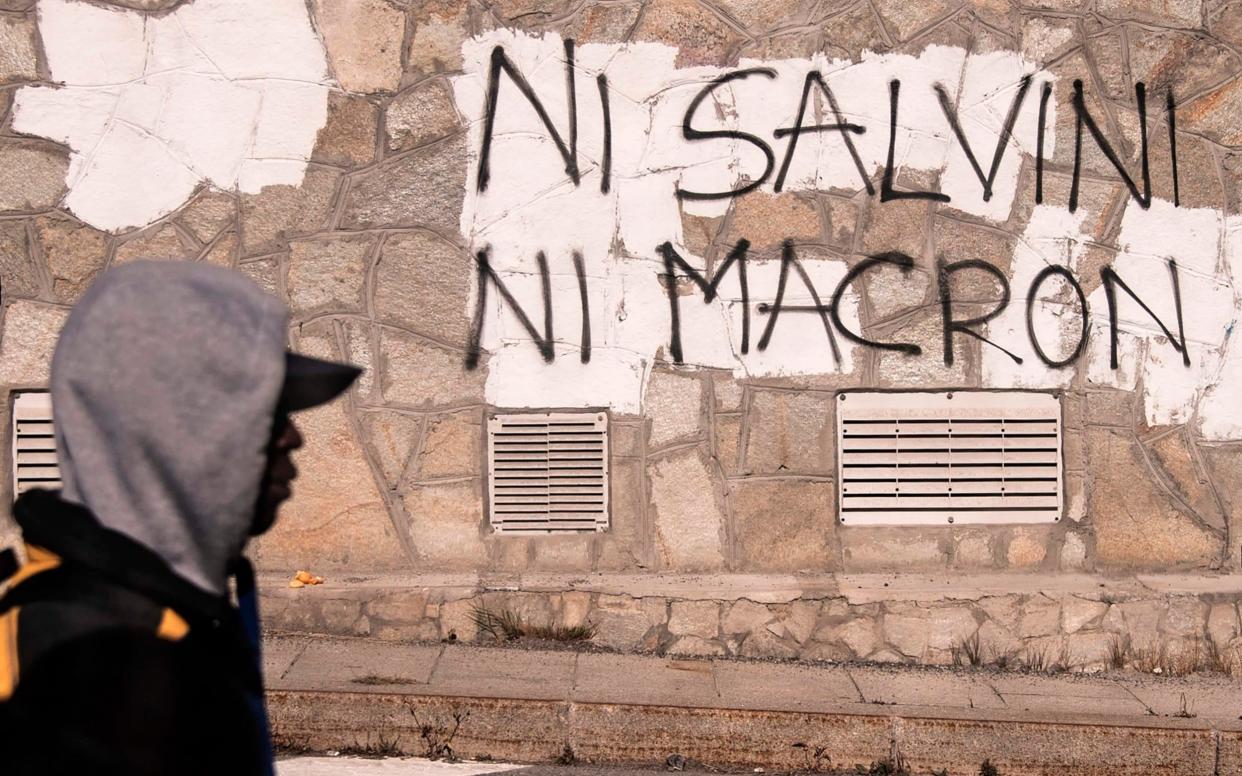 A migrant walks past an inscription reading, in French,