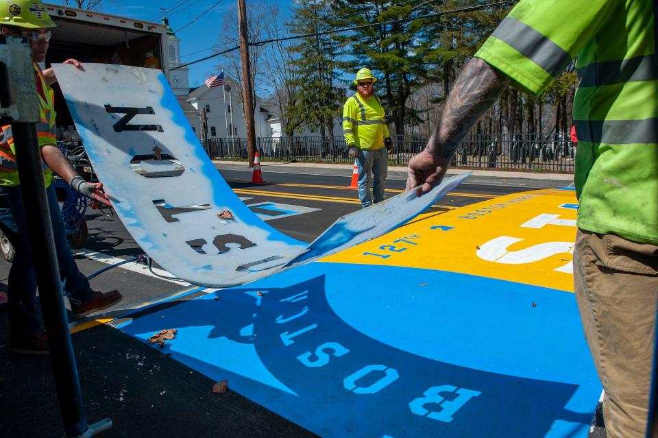 Bryelle Gomes, Errol Charette and James Sawler, all of Road Safe Traffic, lift a Boston stencil while painting the start line for the 127th running of the Boston Marathon on Main Street (Route 135) in Hopkinton, April 11, 2023.