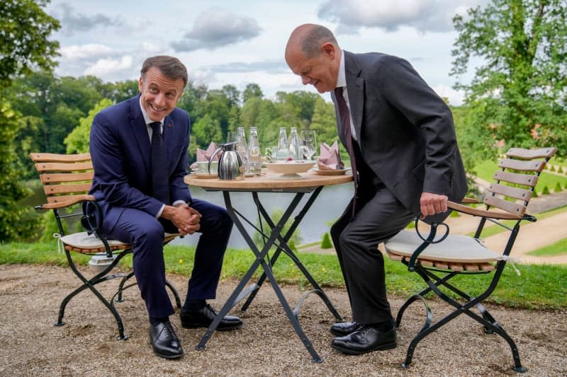 German Chancellor Olaf Scholz (R) and French President Emmanuel Macron sit at a table in the garden of Schloss Meseberg, the guesthouse of the Germab government, ahead of the French-German Council of Ministers.  Ebrahim Noroozi/Pool AP/dpa