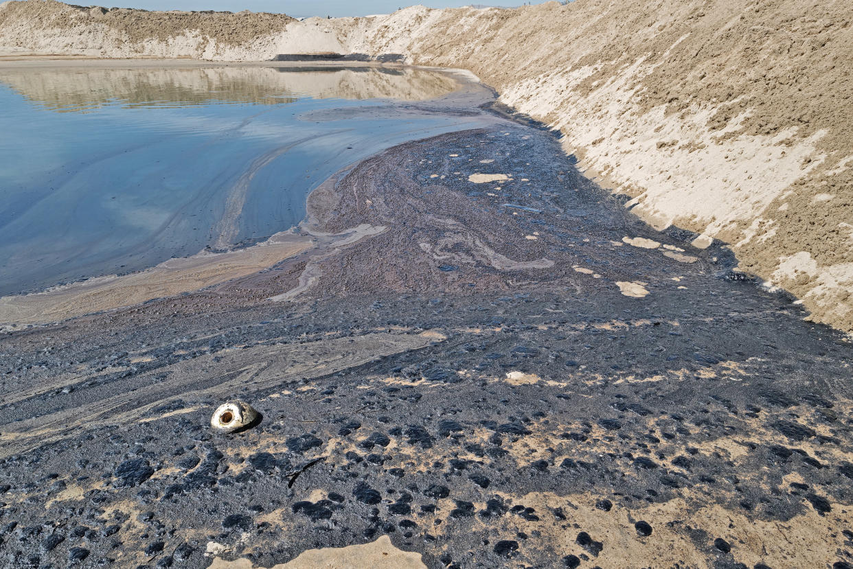 Oil floating on water where it meets a sandy embankment.