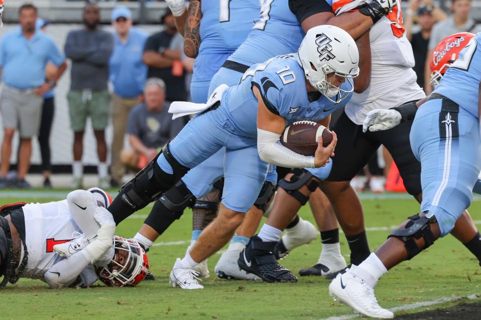 Nov 11, 2023; Orlando, Florida, USA; UCF Knights quarterback John Rhys Plumlee (10) carries the ball Oklahoma State Cowboys linebacker Xavier Benson (1) during the first quarter at FBC Mortgage Stadium. Mandatory Credit: Mike Watters-USA TODAY Sports