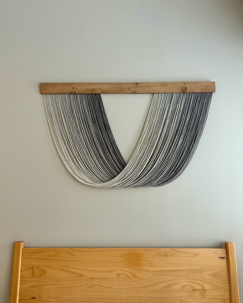 Textile art piece hanging above bed in studio apartment.