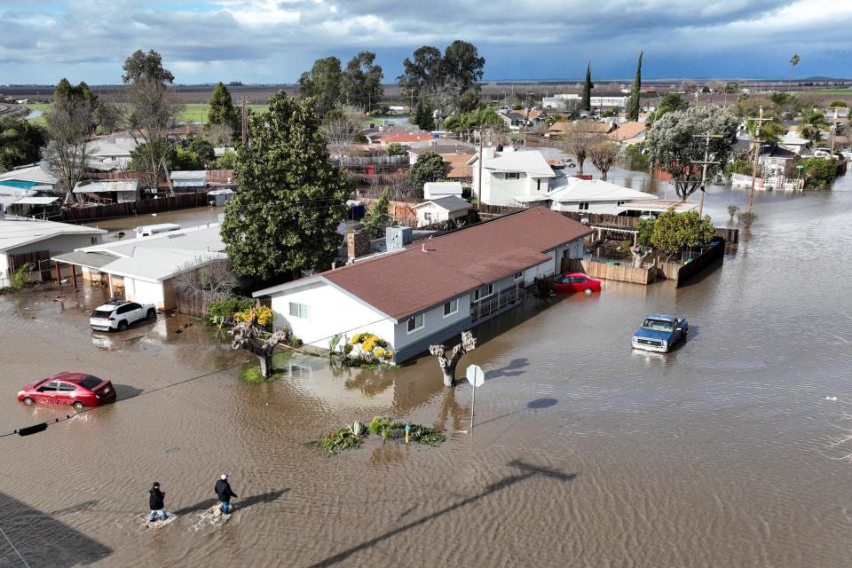 This aerial view shows residents navigating their flooded town in Planada, California, as an "atmospheric river" continues on January 10, 2023. - Relentless storms were ravaging California again Tuesday, the latest bout of extreme weather that has left 14 people dead. Fierce storms caused flash flooding, closed key highways, toppled trees and swept away drivers and passengers -- reportedly including a five-year-old-boy who remains missing in central California.