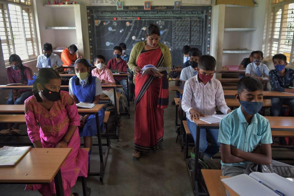 A teacher walks down an aisle between students at desks.