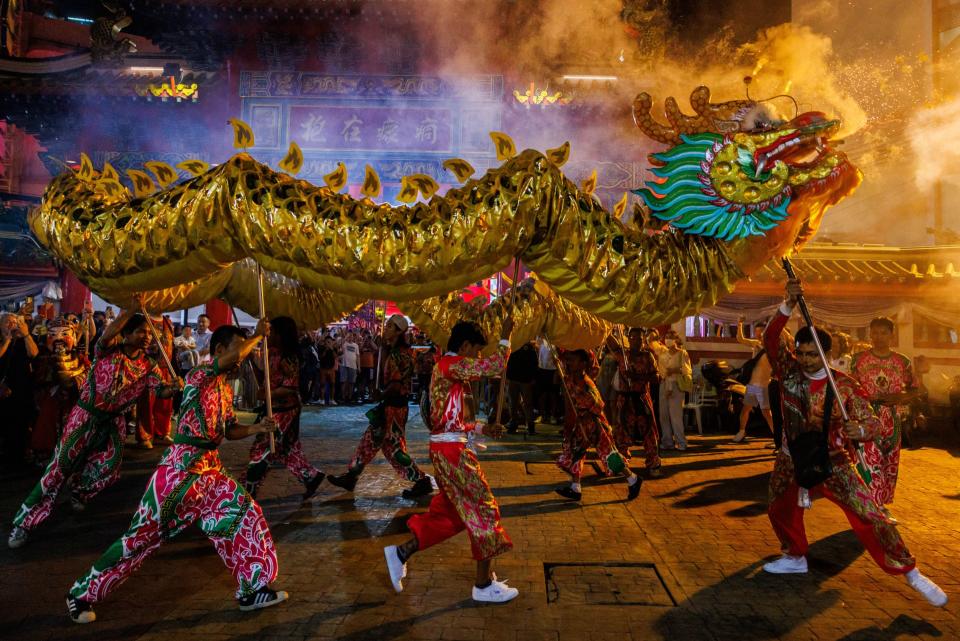 people in red silk outfits walk through a crowded city street while holding up a large dragon puppet