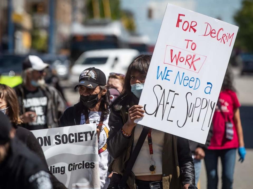 A woman holds a sign calling for a safe supply of drugs to accompany any decriminalization efforts, at a protest in Vancouver on May 11, 2021. Many harm reduction advocates say a safe and regulated supply of drugs is the only way to prevent more Canadians dying from toxic street drugs. (Darryl Dyck/The Canadian Press - image credit)