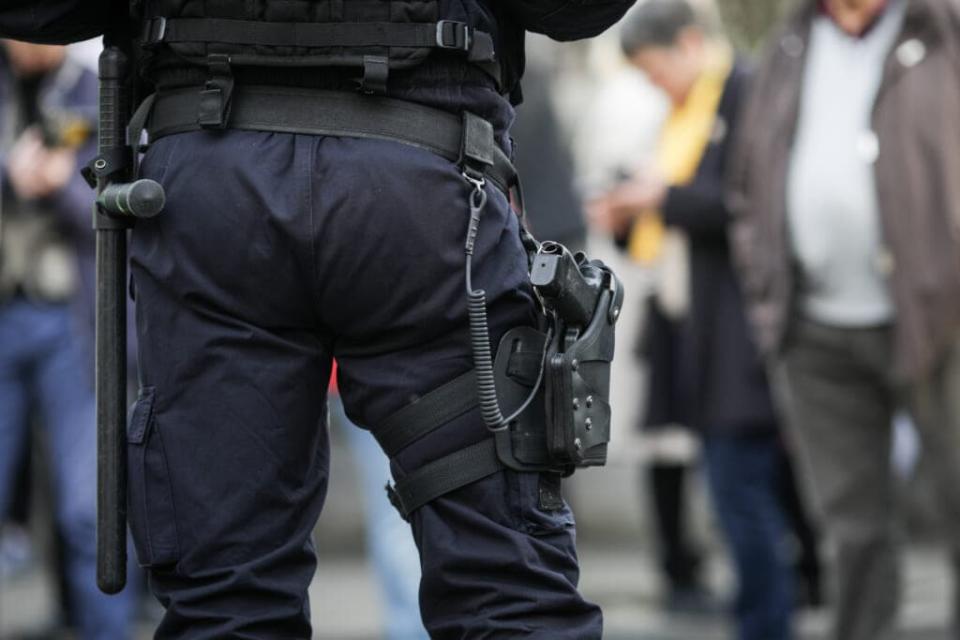 Details of the security kit of a riot police officer (including handcuffs, 9mm handgun, radio station and baton) sitting amongst civilians