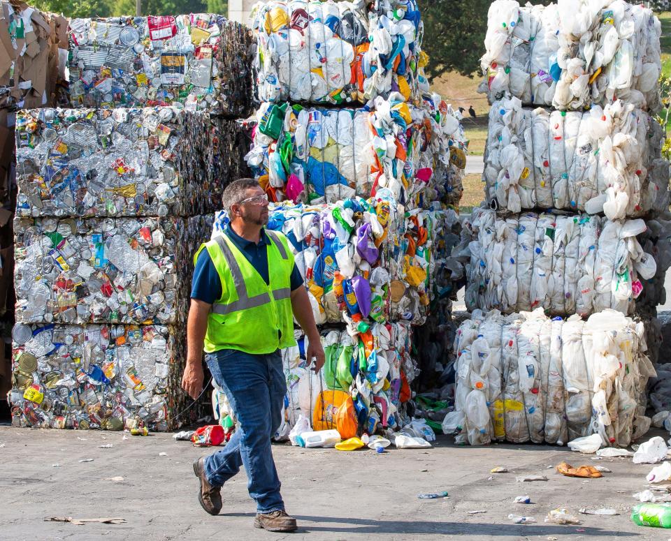 A worker walks past bales of recycled plastic bottles, aluminum and paper at the Leveda Brown Environmental Park and Transfer Station in Gainesville.