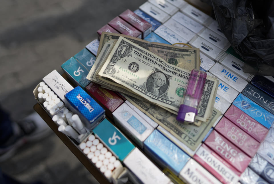 U.S. dollar bills, belonging to a street vendor, sit atop cigarettes for sale in Caracas, Venezuela, Friday, Oct. 1, 2021. A new currency with six fewer zeros debuts today in Venezuela, whose currency has been made nearly worthless by years of the world's worst inflation. The new currency tops out at 100 bolivars, a little less than $25 until inflation starts to eat away at that as well. (AP Photo/Ariana Cubillos)