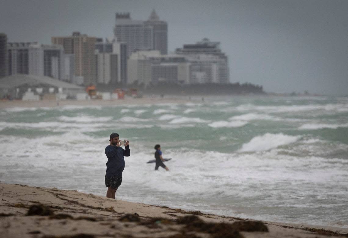 A man takes a photo of surfers and the waves during bad weather on Wednesday, Dec. 13, 2023, in South Miami Beach. Alie Skowronski/askowronski@miamiherald.com