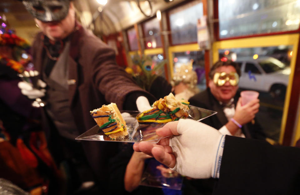 Members of the "Societe des Champs Elysee" pass out king cake as they ride the Rampart-St. Claude street car line, which just opened last fall, to commemorate the official start of Mardi Gras season, in New Orleans, Friday, Jan. 6, 2017. Wearing masks and festive costumes, they honored their king and queen at a neighborhood bar and danced as a brass band played "Carnival Time," before boarding their red street car. (AP Photo/Gerald Herbert)