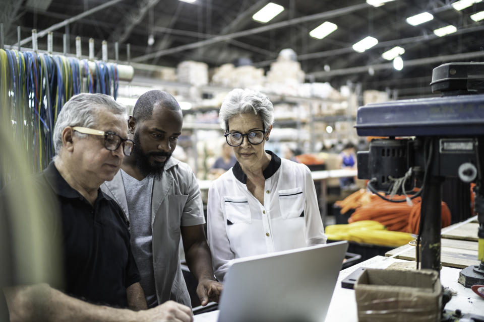 Coworkers using laptop and working together in factory