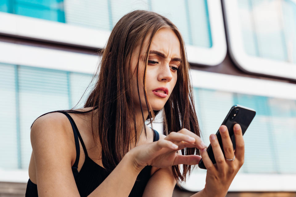 Reading Bad News on Mobile Phone. Young teenage woman checking her messages and social media post on her mobile phone. Looking worried and questioning reading the bad news and messages on her smart phone. Urban Young Generation Social Media Lifestyle Portrait.