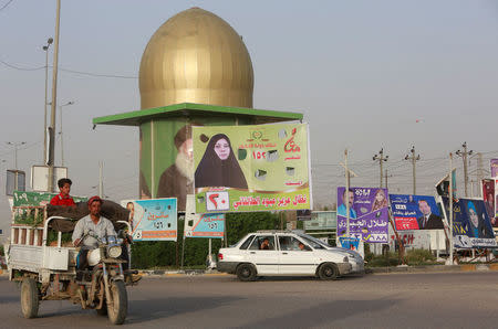 Vehicles drive near campaign posters of candidates ahead of parliamentary election, in Najaf, Iraq, April 20, 2018. REUTERS/Alaa Al-Marjani