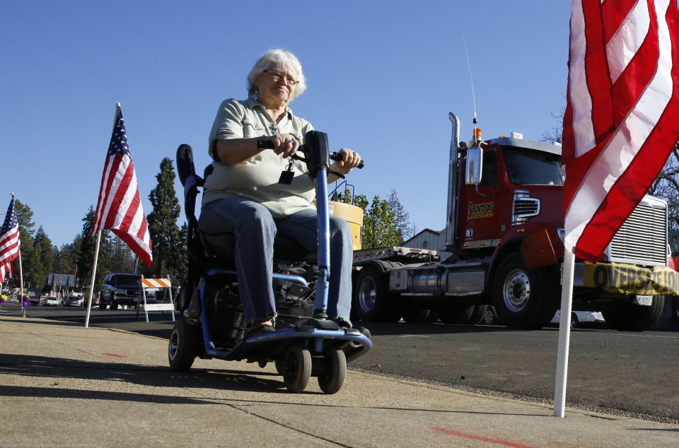 Roxanne Mulder passes flags lining the streets Friday, Nov. 8, 2019m in Paradise, Calif, that were placed in remembrance of last years Camp Fire, Friday marks the one year anniversary of the wildfire that nearly destroyed the entire town. Mulder's home survived the fire when firefighters used the water in her swimming pool to protect the house. (AP Photo/Rich Pedroncelli)