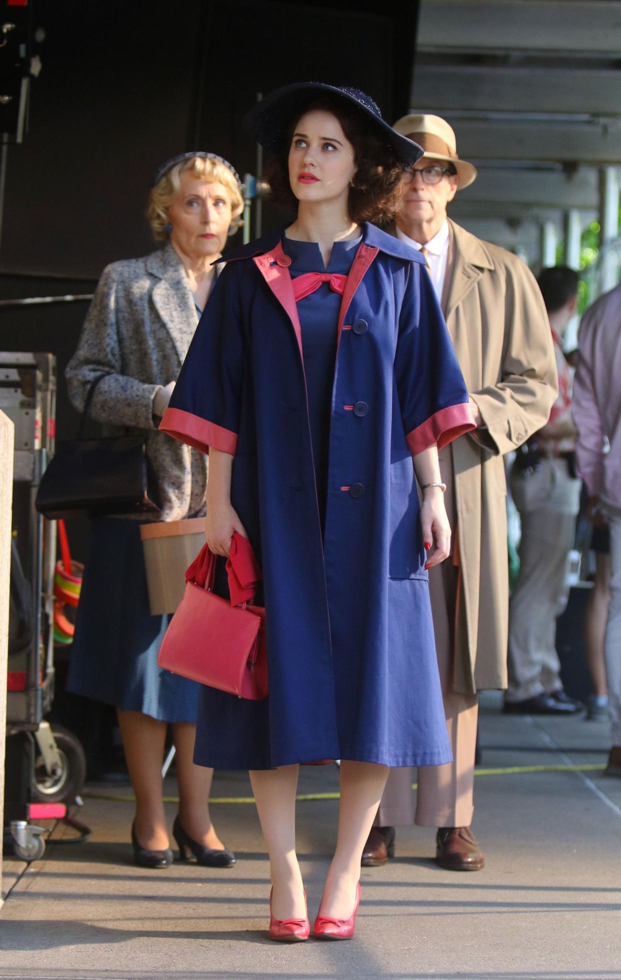 Rachel Brosnahan looks radiant in a navy blue and pink coat and dress, with matching accessories, while filming a scene for "The Marvelous Mrs. Maisel" in New York City on Aug. 15, 2019.