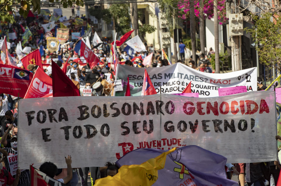 Demonstrators march holding a banner with a message that reads in Portuguese; "Get out genocidal Bolsonaro and all your government" during a protest against Brazilian President Jair Bolsonaro and his handling of the pandemic and economic policies protesters say harm the interests of the poor and working class, in Cuiaba, Brazil, Saturday, June 19, 2021. (AP Photo/Andre Penner)