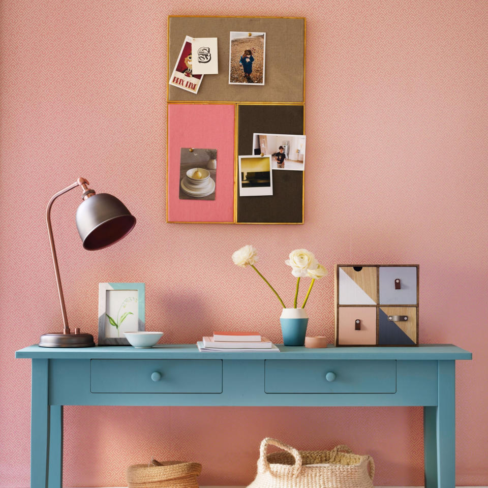 White and pink wall and rug, with corkboard and baby blue sideboard covered in objects in shades of blue, pink, yellow, and orange