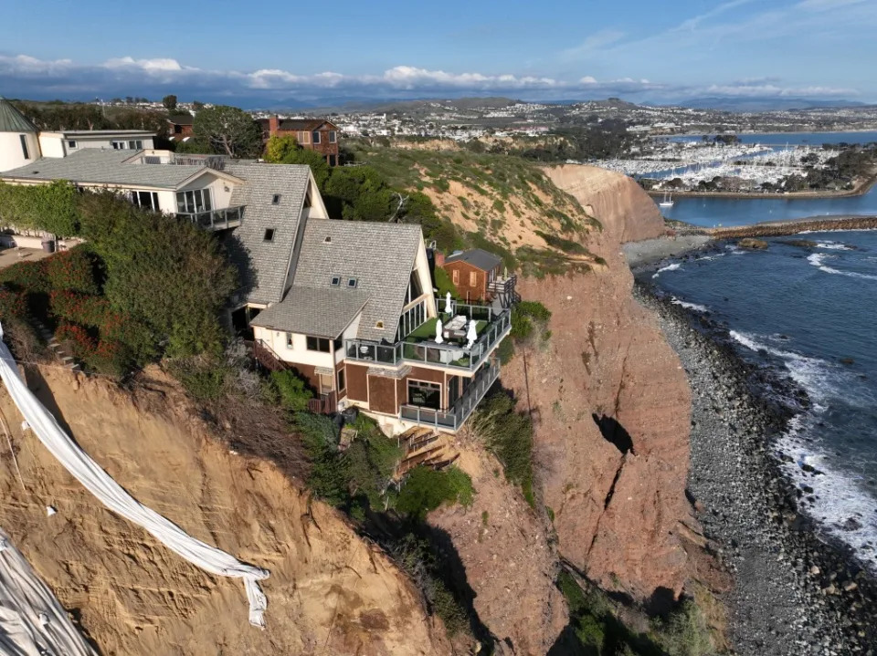 An aerial view of a double A-frame cliff-side mansion, between two other mansions affected by a landslide and protective tarps to protect from further slides, from upcoming storms in Dana Point Tuesday, Feb. 27, 2024. Los Angeles Times via Getty Images