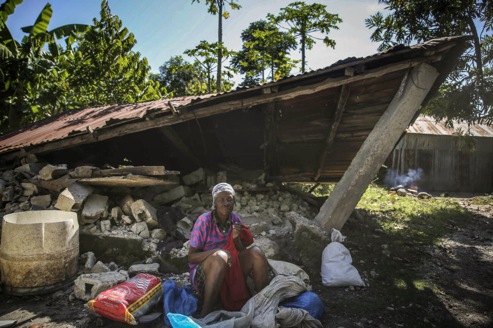 A woman sits in front of a destroyed house after the earthquake in Camp-Perrin, Les Cayes, Haiti, Sunday, Aug. 15, 2021. The death toll from the magnitude 7.2 earthquake in Haiti soared on Sunday as rescuers raced to find survivors amid the rubble ahead of a potential deluge from an approaching tropical storm. (AP Photo/Joseph Odelyn)