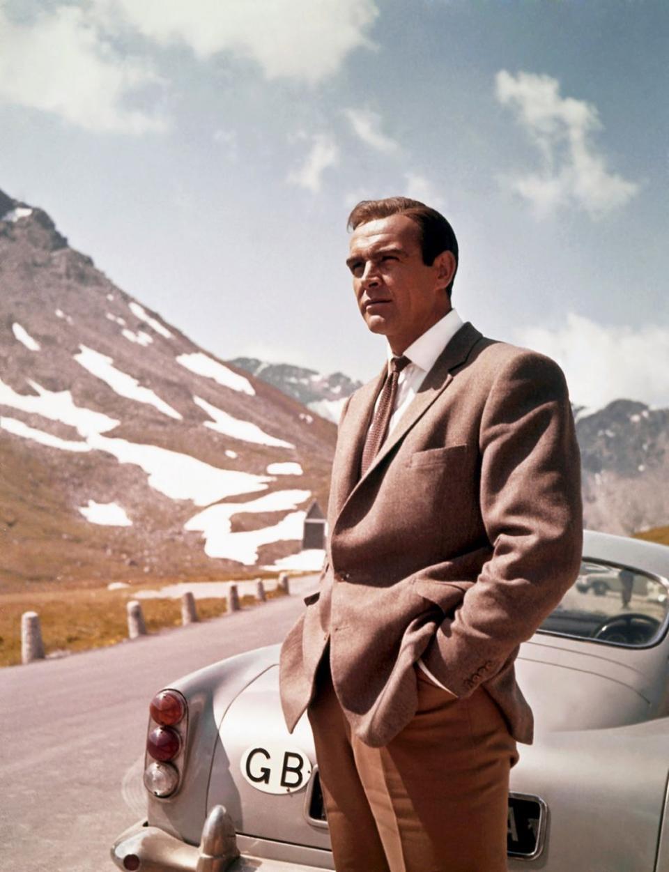 <p>Next to his Aston Martin DB5 in a scene from <em>Goldfinger</em>. </p>