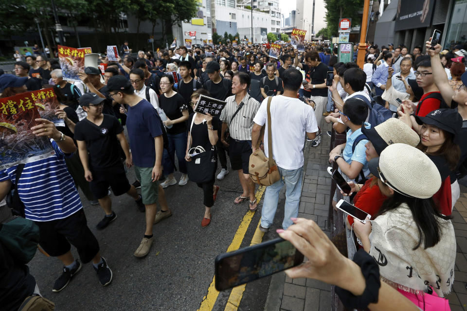 In this July 7, 2019, photo, mainland Chinese tourists, right, watch and film the protesters with placards march on a street in Hong Kong. It's still the world's "freest" economy, one of the biggest global financial centers and a scenic haven for tycoons and tourists, but the waves of protests rocking Hong Kong are exposing strains unlikely to dissipate as communist-ruled Beijing's influence grows. (AP Photo/Andy Wong)