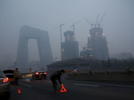 A man sets up a warning sign next to a vehicle after an accident amid heavy smog after the city issued its first ever "red alert" for air pollution, in Beijing, China, December 8, 2015. REUTERS/Kim Kyung-Hoon