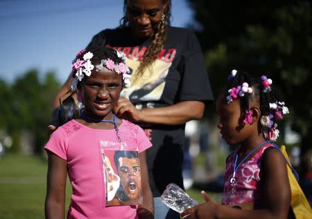 Jamani Booker, 6, (R) and Ramiya Taylor, 6, get lanyards from their grandmother showing an image of Muhammad Ali during the funeral procession. REUTERS/Lucy Nicholson