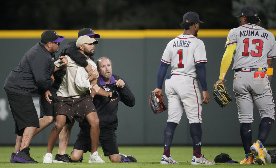 Field guards hold onto a fan as he tries to reach Atlanta Braves right fielder Ronald Acuna Jr., right, while second baseman Ozzie Albies (1) looks on in the seventh inning of a baseball game against the Colorado Rockies, Monday, Aug. 28, 2023, in Denver. (AP Photo/David Zalubowski)