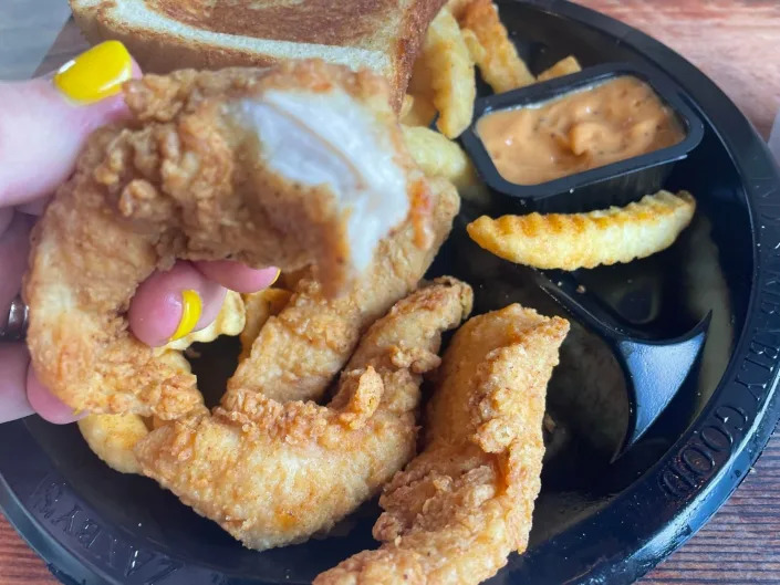 The writer holds a chicken finger with visible white meat in front of a plate of chicken fingers at Zaxby's