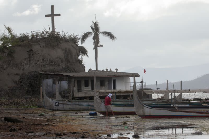 A man cleans his boat in an ash-covered fishing port in Talisay