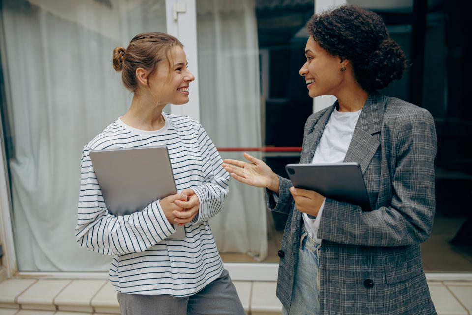 Two professionals engaging in a cheerful discussion, one holding a laptop, the other a tablet