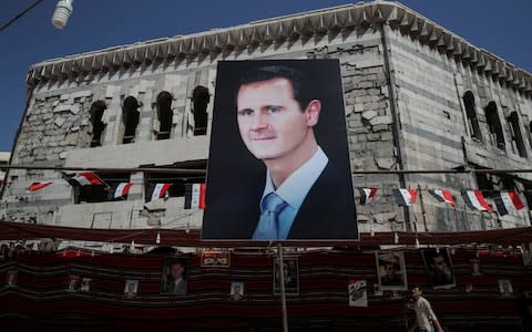 A man walks past a banner depicting Syrian president Bashar al-Assad in former opposition stronghold Douma, outside Damascus, - Credit: Reuters