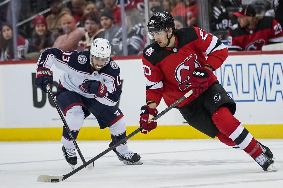 New Jersey Devils' Michael McLeod (20) skates with the puck around Columbus Blue Jackets left wing Johnny Gaudreau (13) during the third period of an NHL hockey game Sunday, Oct. 30, 2022, in Newark, N.J. (AP Photo/Eduardo Munoz Alvarez)