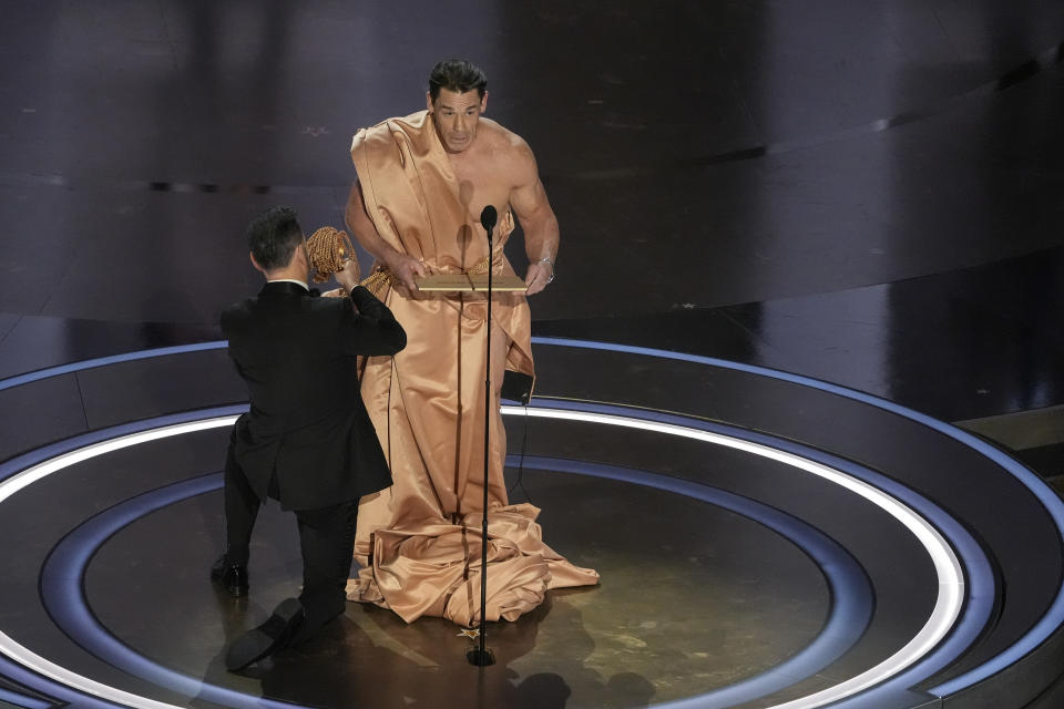 John Cena presents the award for best costume design while Jimmy Kimmel makes him an outfit during the Oscars on Sunday, March 10, 2024, at the Dolby Theatre in Los Angeles. (AP Photo/Chris Pizzello)