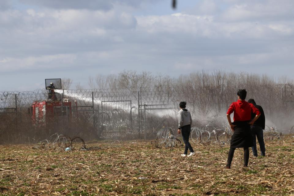 Greek firefighters spray water as migrants stand near a border fence on the Turkish side during clashes with the Greek riot police at the Turkish-Greek border in Pazarkule, Edirne region, on Saturday, March 7, 2020. Thousands of refugees and other migrants have been trying to get into EU member Greece in the past week after Turkey declared that its previously guarded borders with Europe were open. (AP Photo/Darko Bandic)