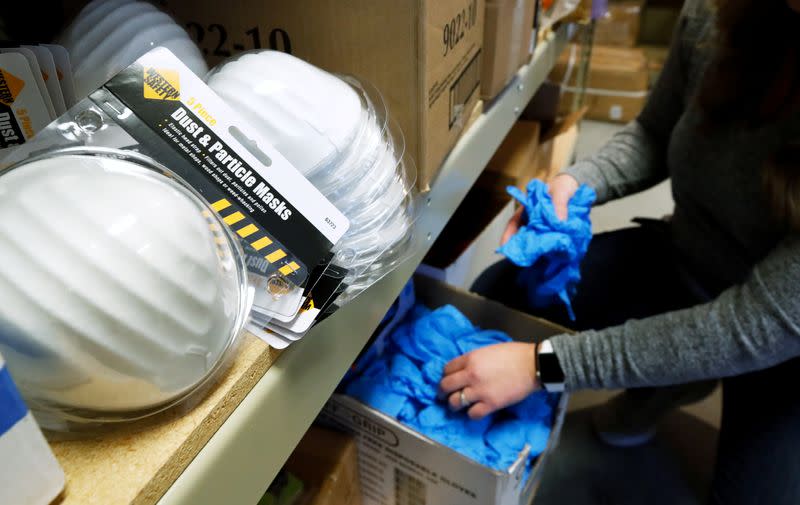 Kristen Curley, owner of Nitro-Pac, grabs some rubber protective gloves as dust & particle mask sit on a shelf that will be part of personal protection and survival equipment kits ordered by customers preparing against novel coronavirus, at Nitro-Pak in Mi