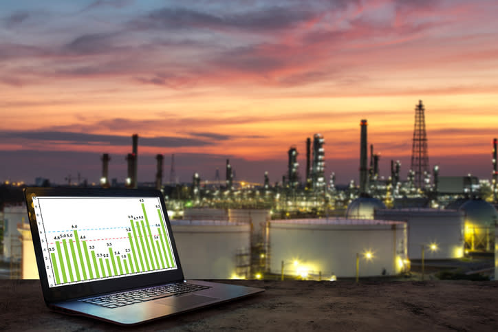 A laptop in the foreground and an oil refinery in the background.